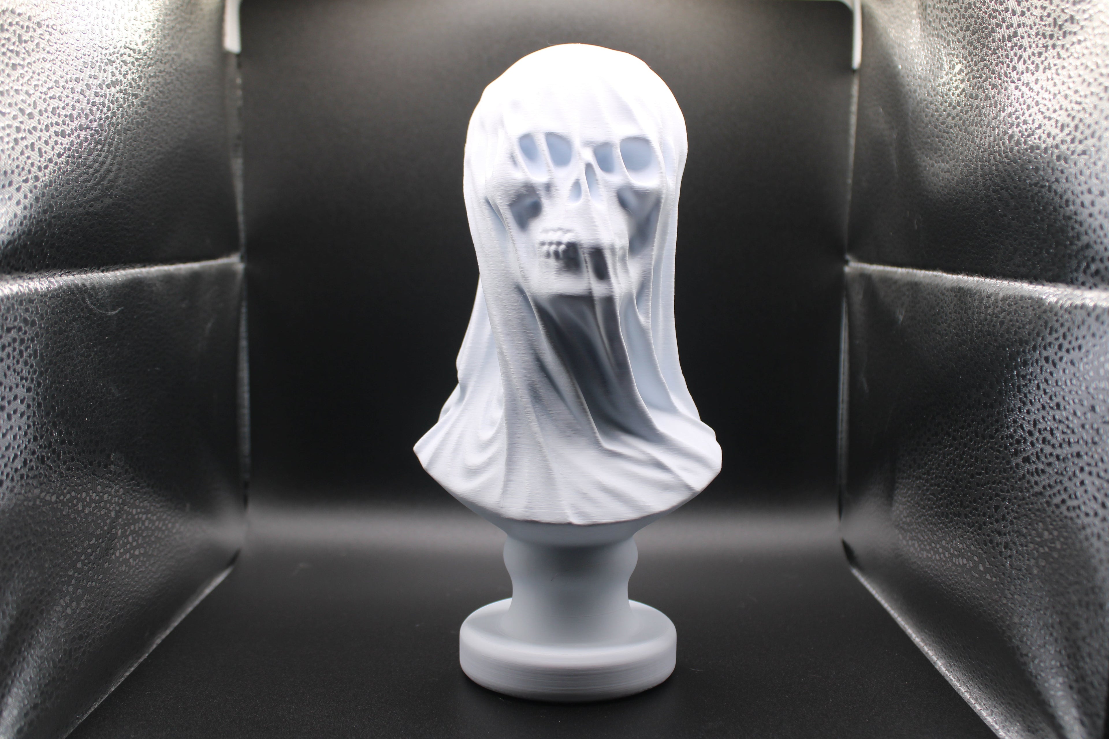 Bust of a ghost with a white sheet draped over it against a black background