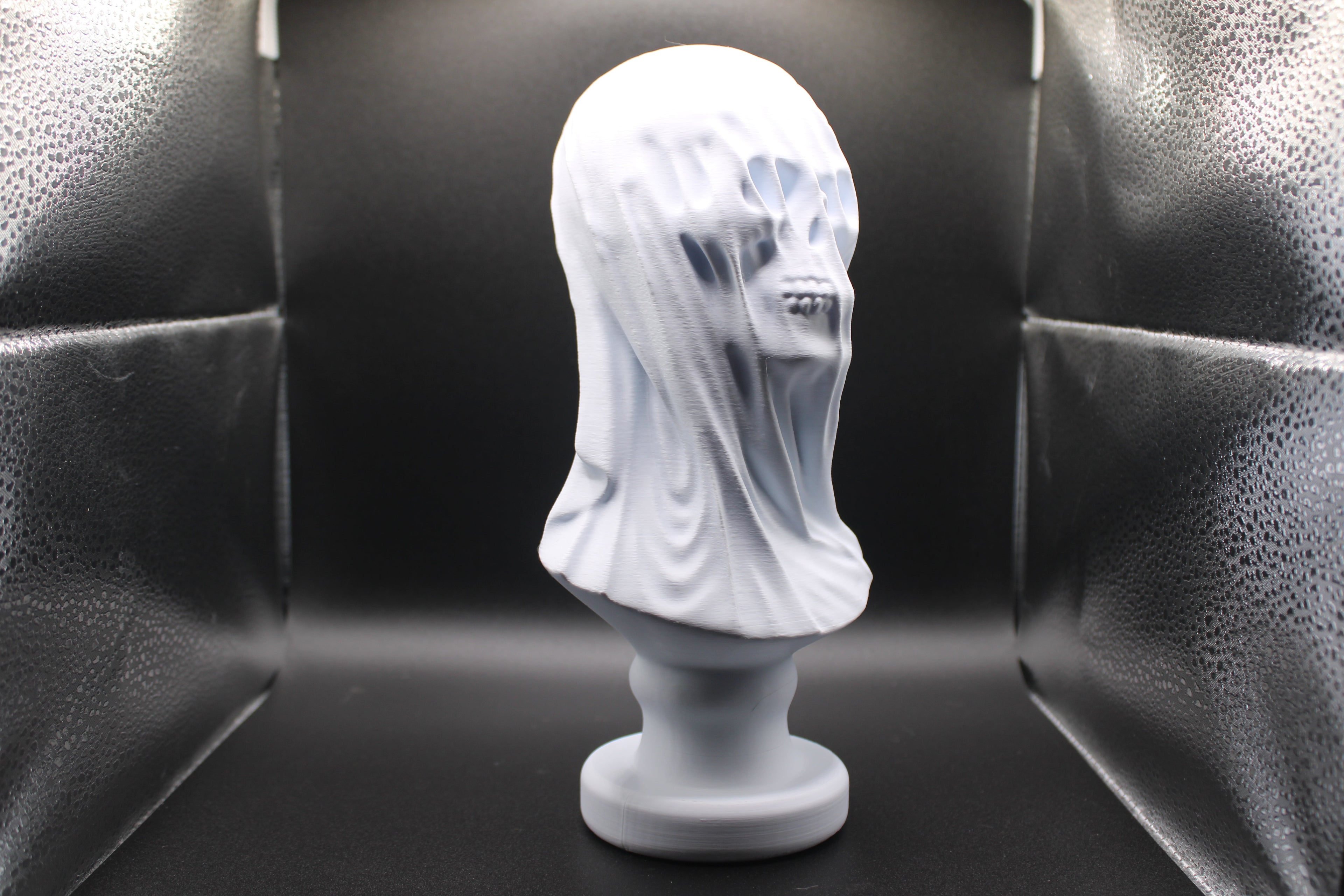 White marble bust of a woman with a veil on a black background
