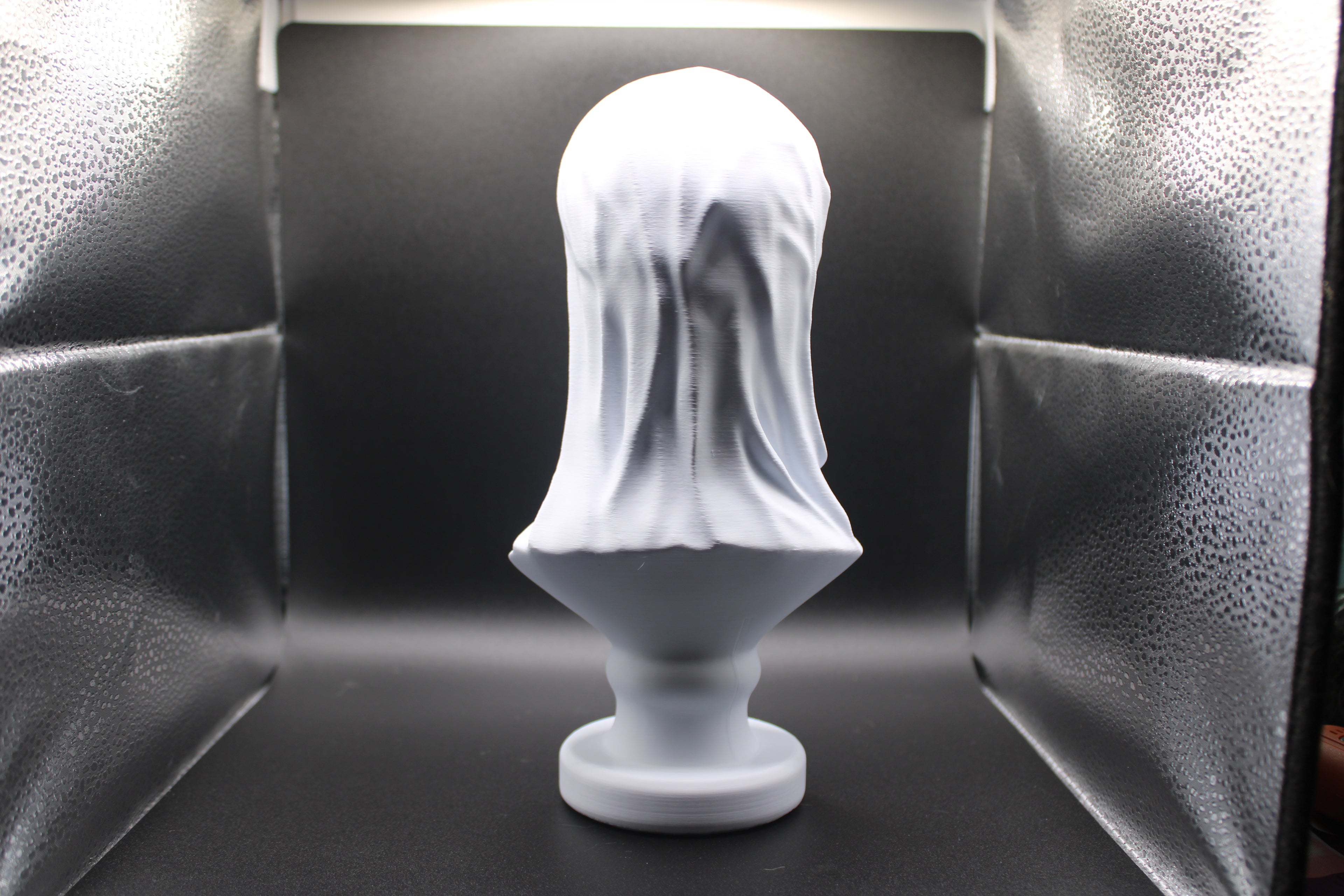 White sculpture of a head with a veil on a black background